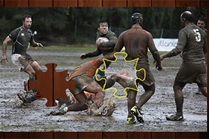 Jucători de rugby murdari de noroi se luptă pentru minge pe un teren noroios, cu un efect de piesă de puzzle evidențiată în imagine