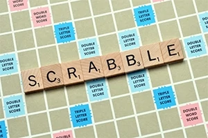 Piese din lemn cu literele formând cuvântul SCRABBLE pe o tablă de joc cu pătrate colorate pentru punctaj